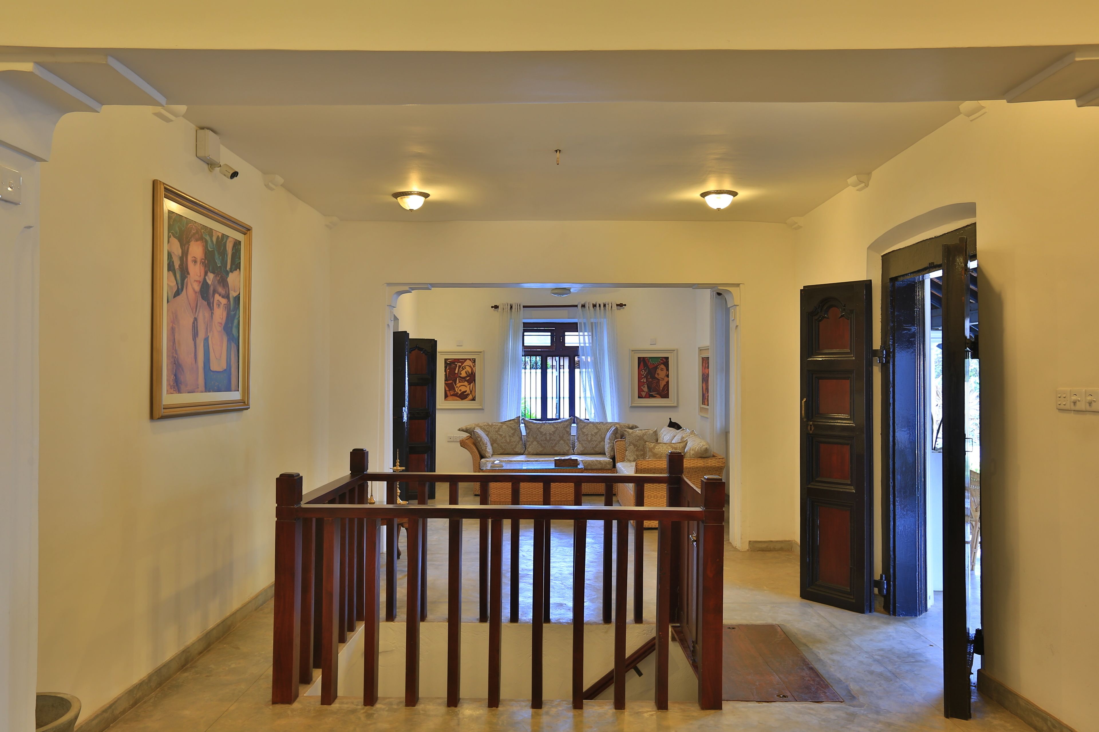 A hallway with a wooden railing, a sofa set, and a door leading to another room.