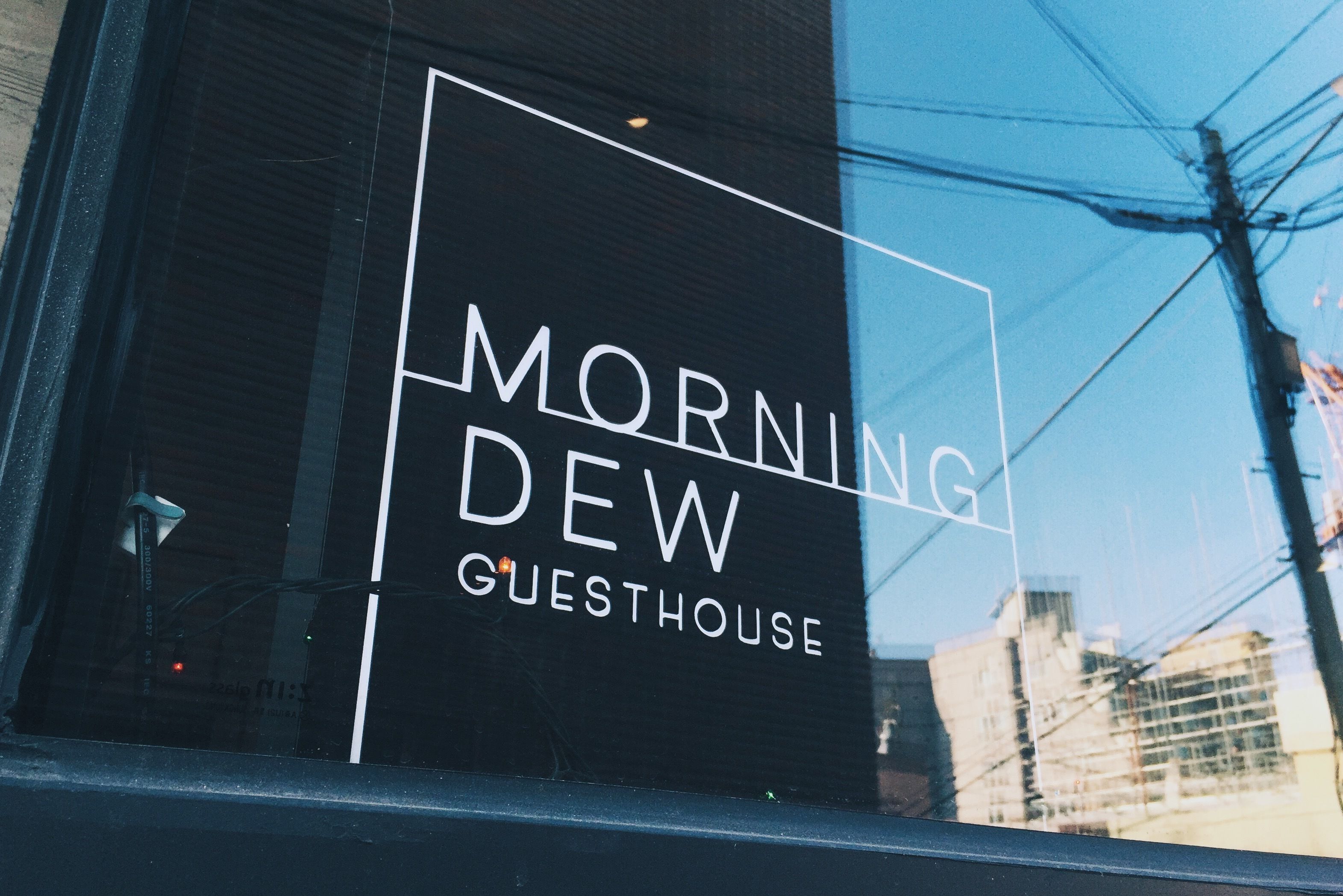 Um letreiro com o texto 'MORNING DEW GUESTHOUSE' sobre um fundo preto.