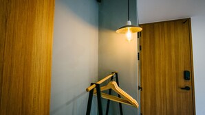 A corner of a room with a wooden door, a wooden hanger stand, and a hanging light fixture. - Morning Dew Guesthouse (Busan)