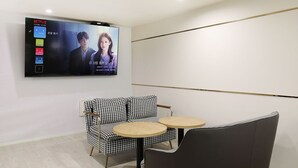 Una habitación moderna con un televisor de pantalla plana montado en la pared reproduciendo una película. Hay una silla con estampado de pied de pavo y una pequeña mesa redonda.