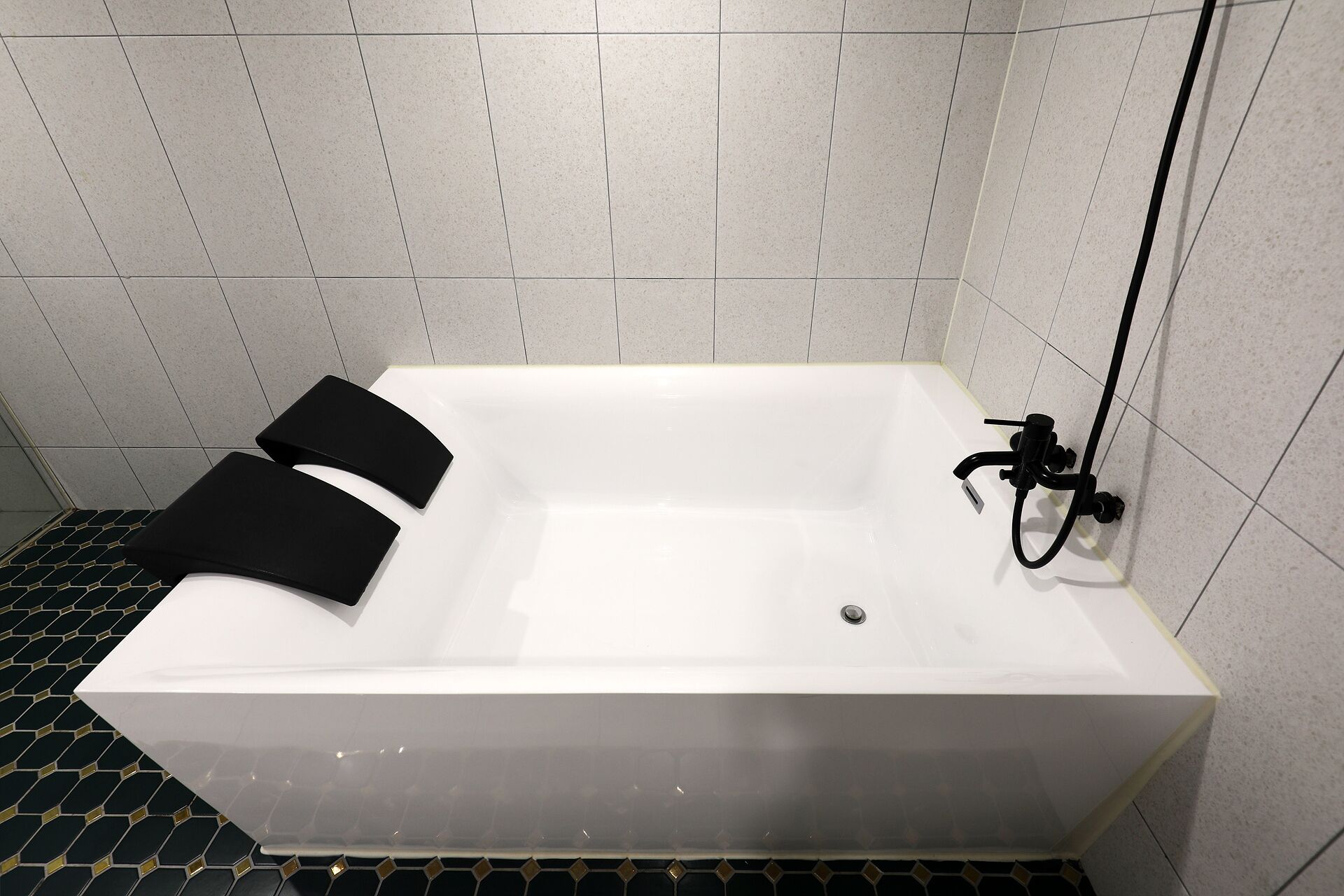 A modern bathroom with a white bathtub, black bath mats, and a shower hose.