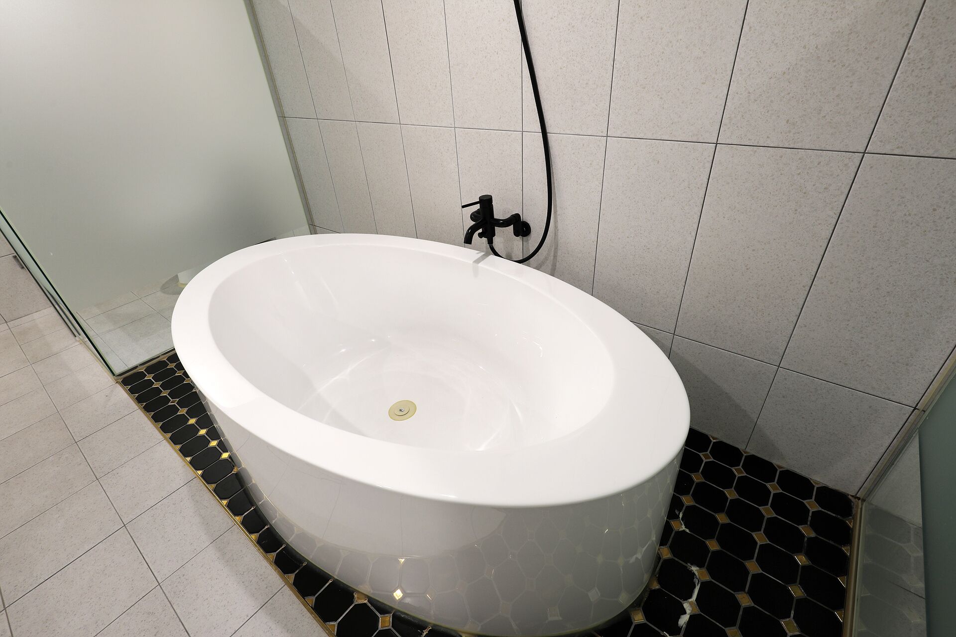 Una bañera blanca grande y separada en un baño con paredes y suelo de baldosas.