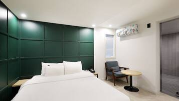 A modern hotel room with a large bed, a small table, a chair, and a window with blinds.