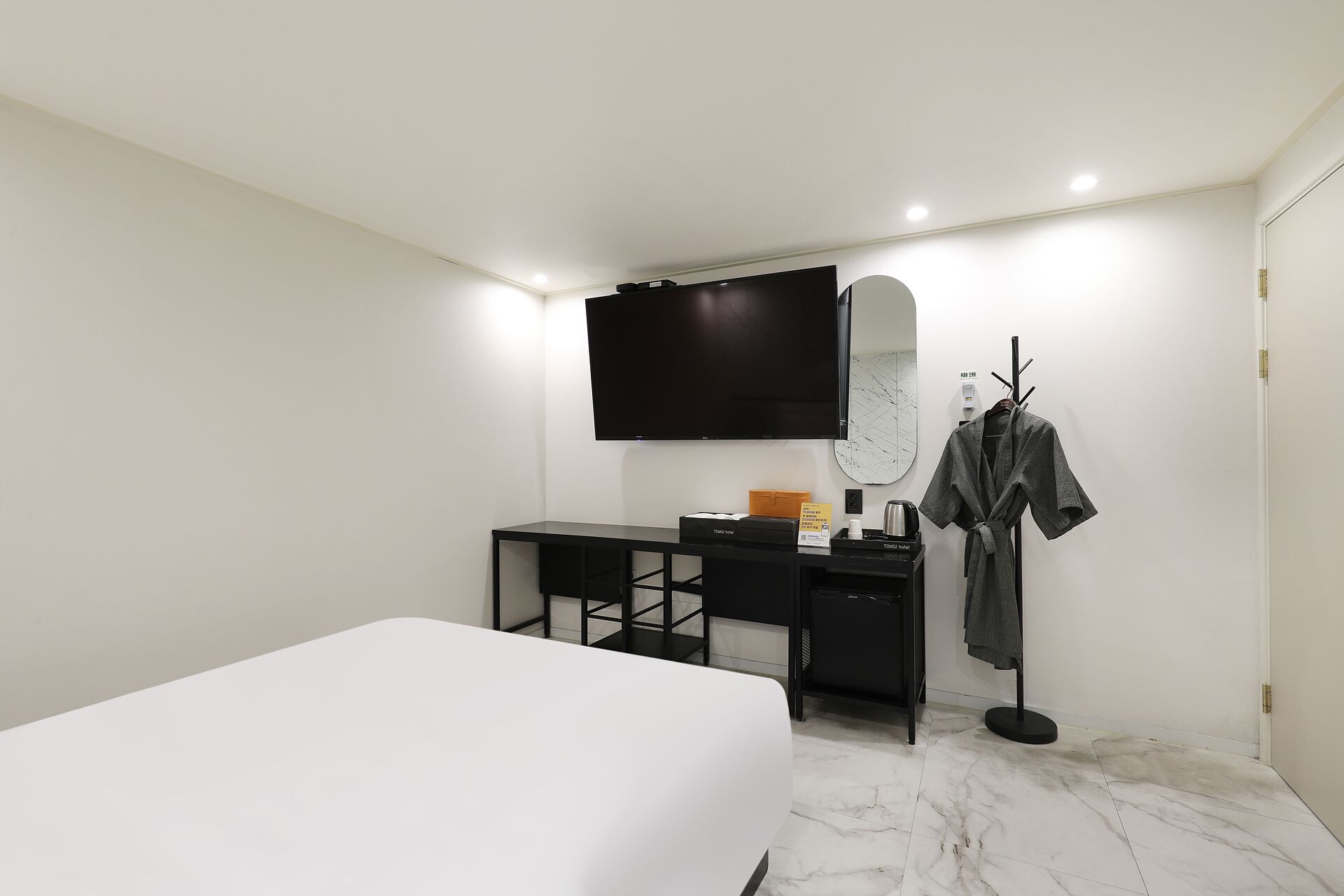 A hotel room with a bed, a desk, a flat-screen TV, a coat rack, and a mirror.
