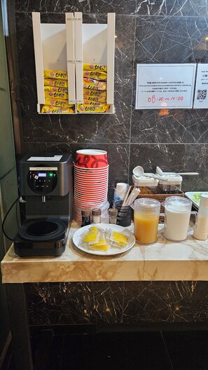 Una barra de desayuno con una cafetera, platos apilados, condimentos y alimentos.