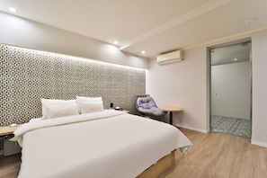 A modern hotel room with a neatly made bed, a chair, a small table, and a shower area.