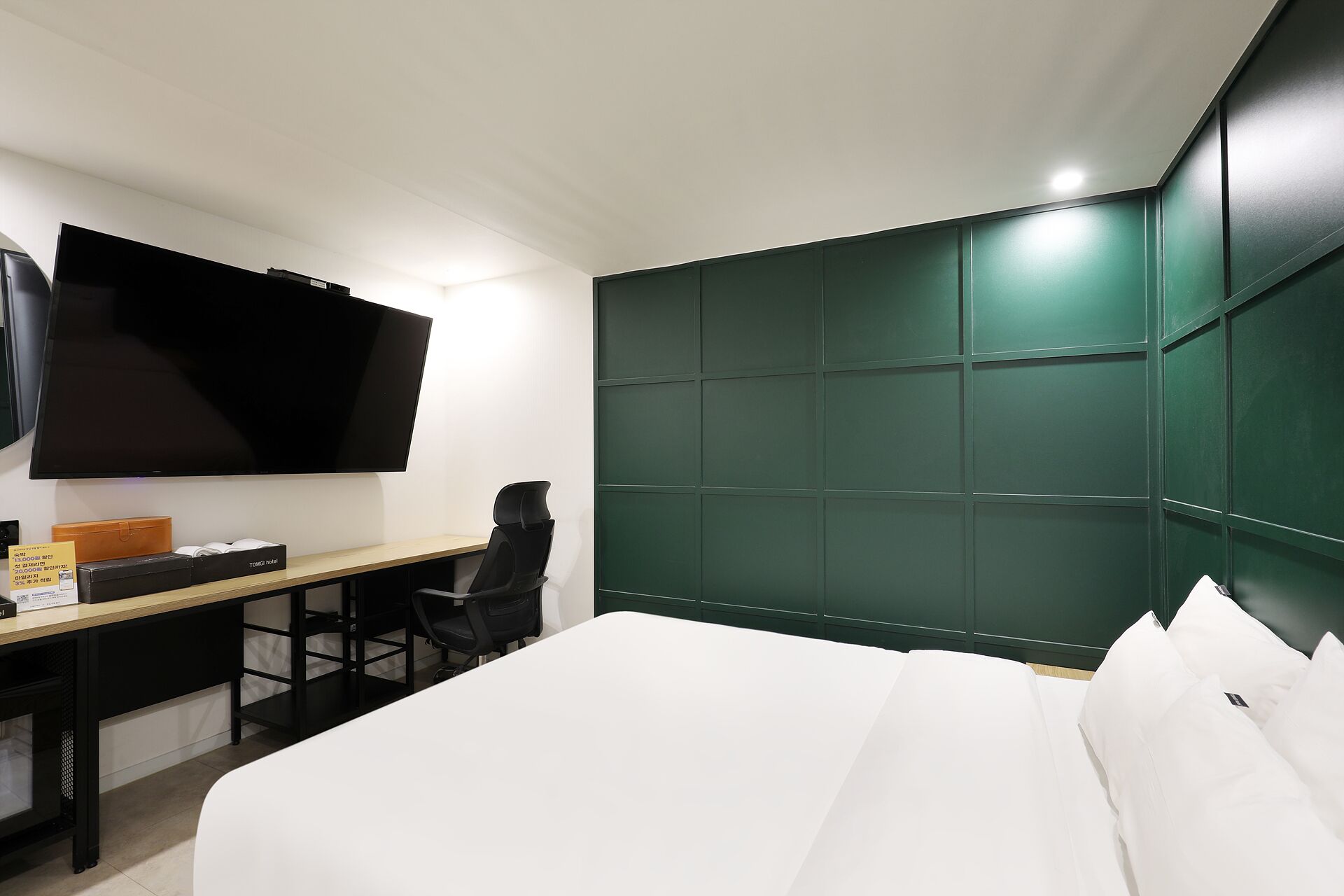 Habitación de hotel con cama, escritorio con silla, televisión de pantalla plana y cabecera verde.