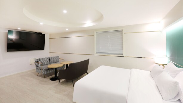 Habitación de hotel con cama, televisión, sofá, una mesita y ventana con persianas.