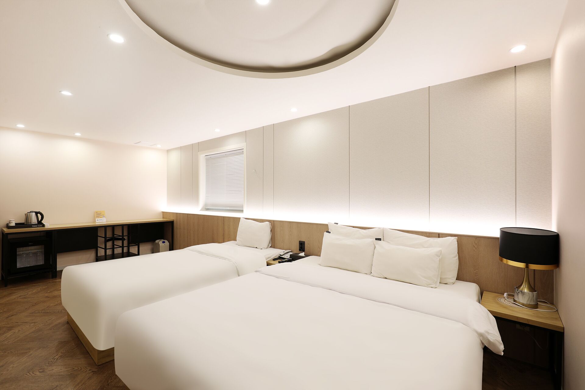 A hotel room with two beds, a desk, a lamp, and a window with blinds.
