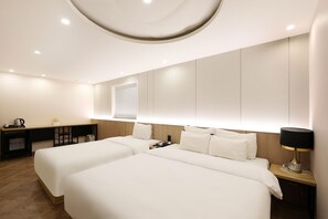 A hotel room with two beds, a desk, a lamp, and a window with blinds. - Hotel Tomgi Jamsil (Seoul)