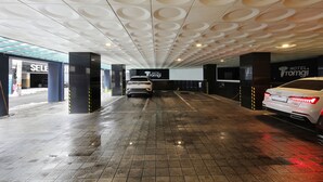 Un garaje para estacionar con un coche blanco en su interior, un letrero que dice 'SELE' y un letrero que dice 'HOTEL TOMIGI'.