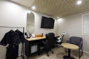 A hotel room with a desk, chair, TV, and a small table.