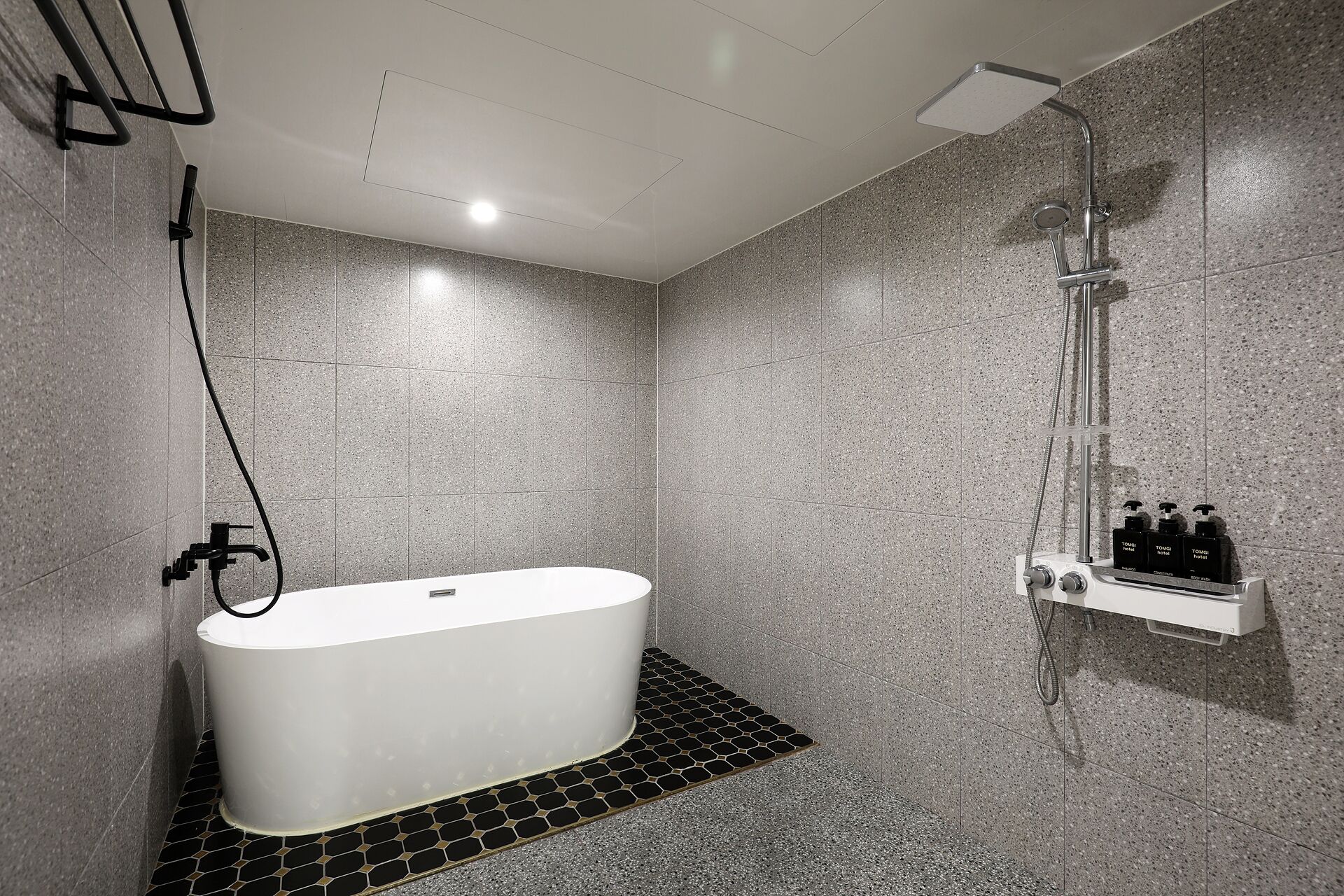 A modern bathroom with a freestanding bathtub, a showerhead, and a soap dispenser on the wall.