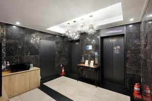A modern elevator with marble walls, a reception desk, and a chandelier. - Hotel Tomgi Jamsil (Seoul)