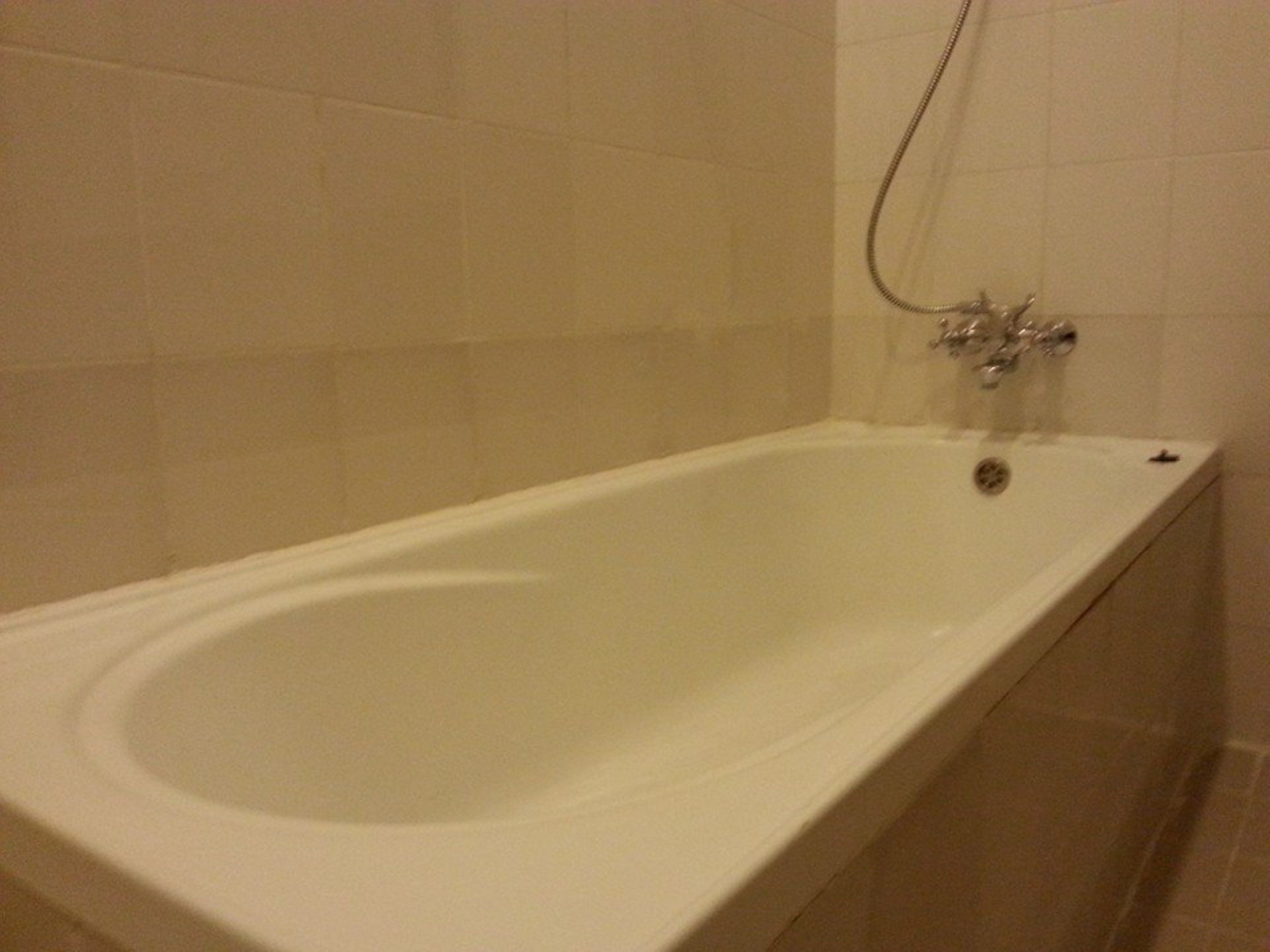 Una bañera blanca estándar con cabezal de ducha y grifo.