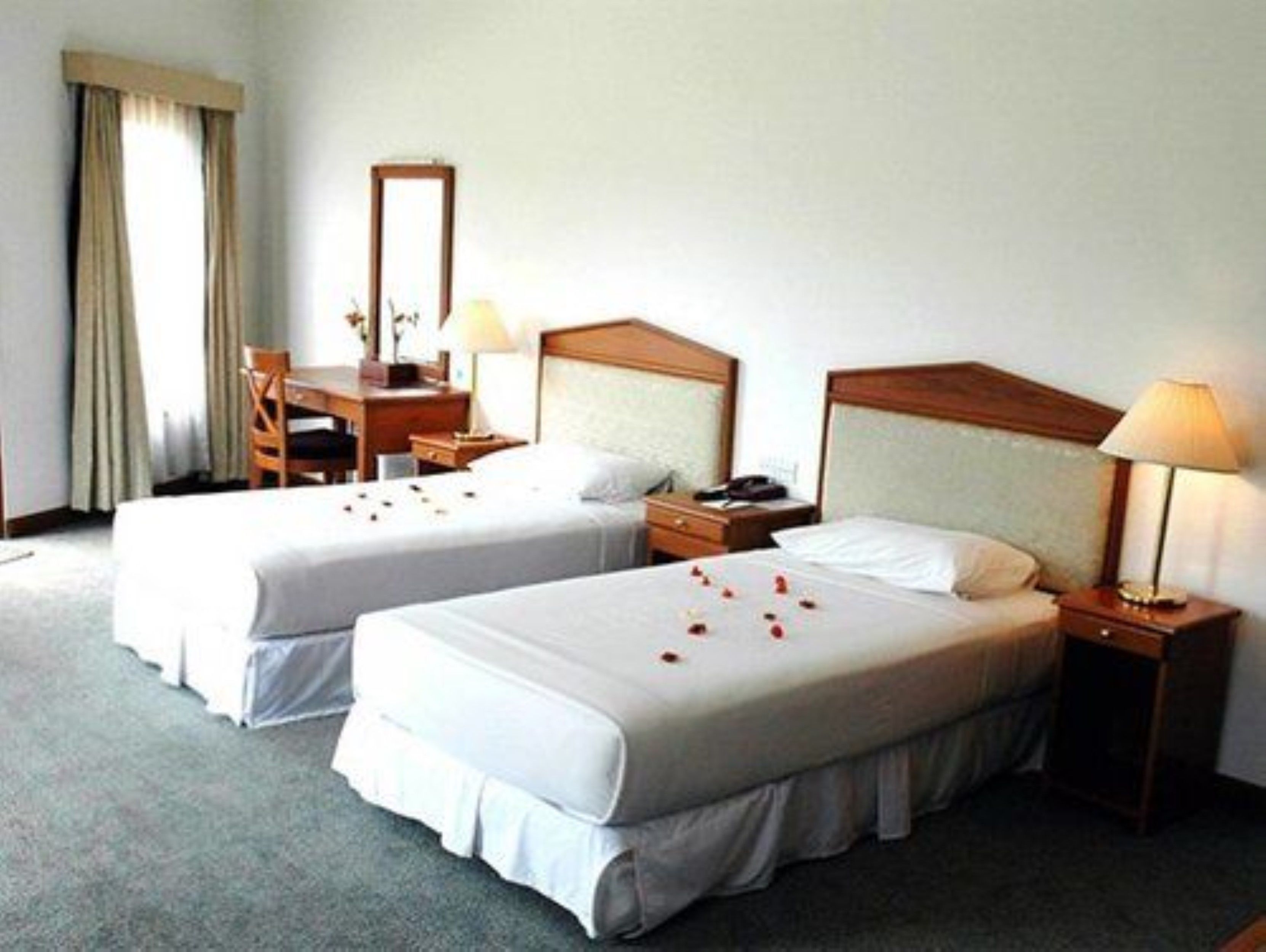 A hotel room with two beds, a desk, a chair, a mirror, and a nightstand with a lamp.