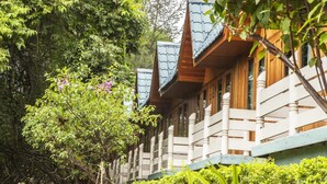 Eine Holzhütte mit Balkon, umgeben von üppiger Vegetation und Bäumen.