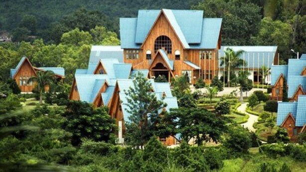 Ein Resort mit mehreren Holzhütten mit blauen Dächern, umgeben von üppigem Grün und Hügeln.
