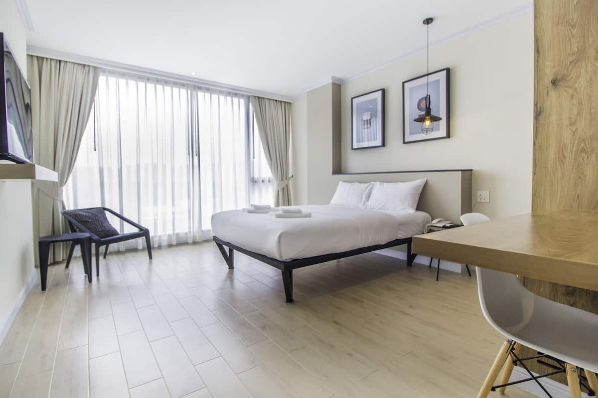 A modern hotel room with a large bed, a desk, a chair, and a TV.