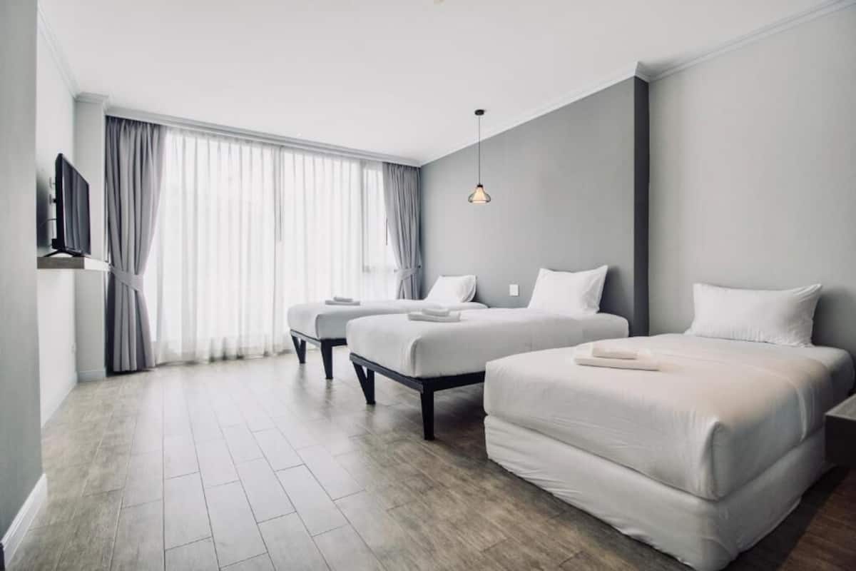 A modern hotel room with two beds, a TV, and a large window with curtains.