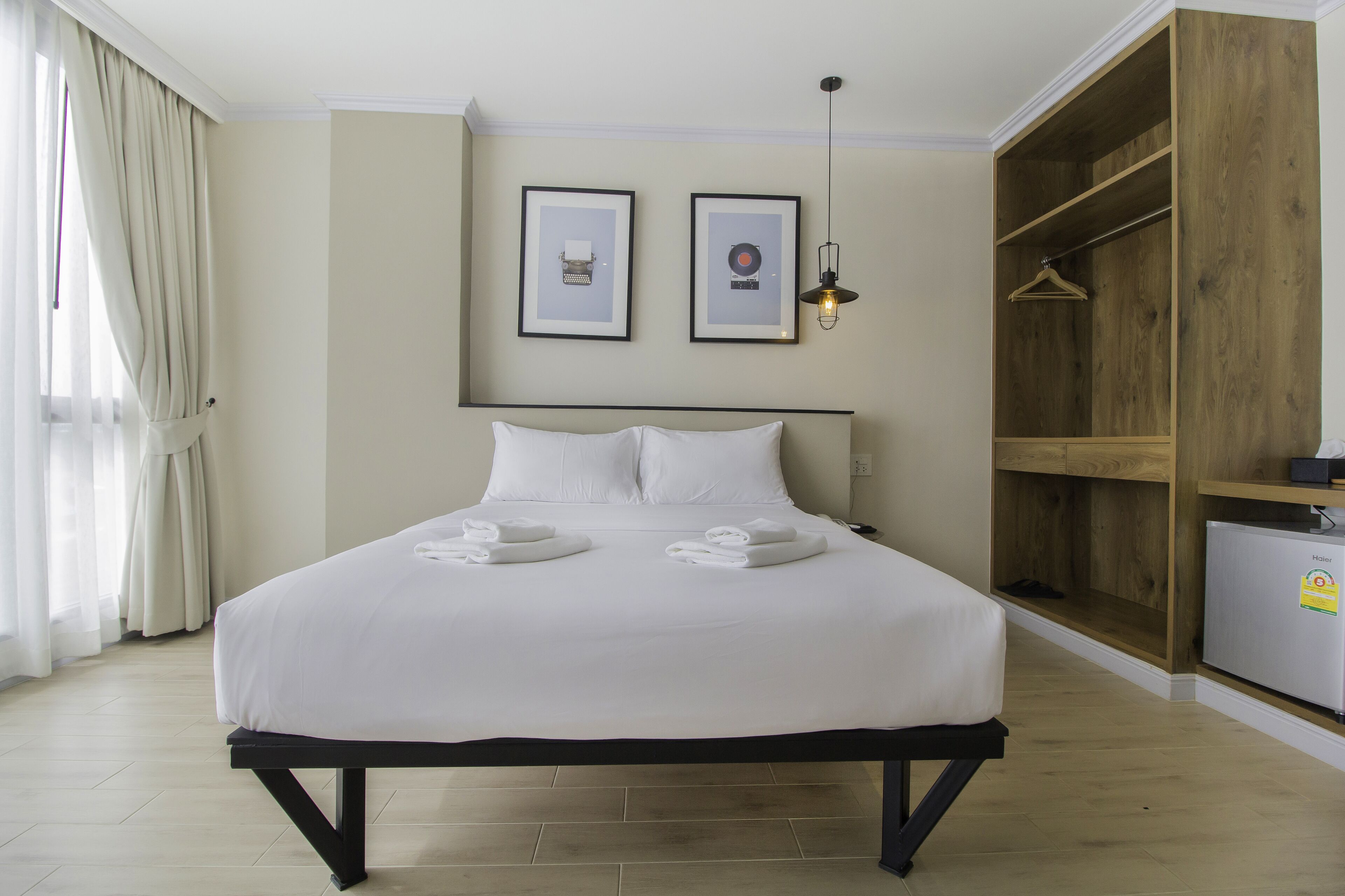 A neatly made bed with white linens and towels, a wooden wardrobe, and two framed pictures on the wall.