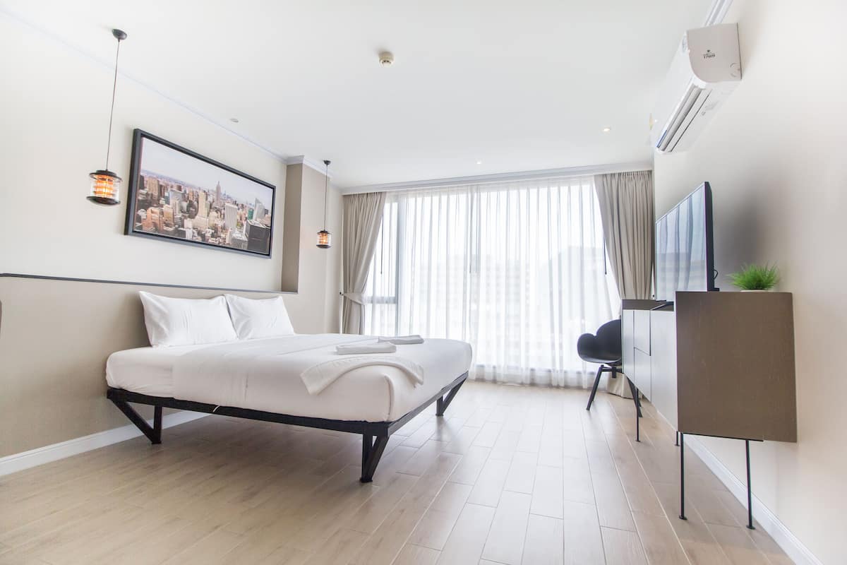 A modern hotel room with a large bed, a flat-screen TV, and a cityscape view.