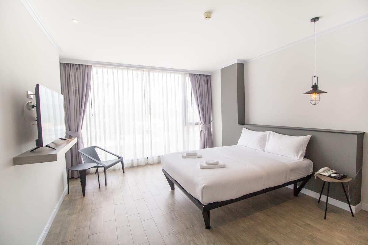 A modern hotel room with a large bed, a desk, a chair, and a television.