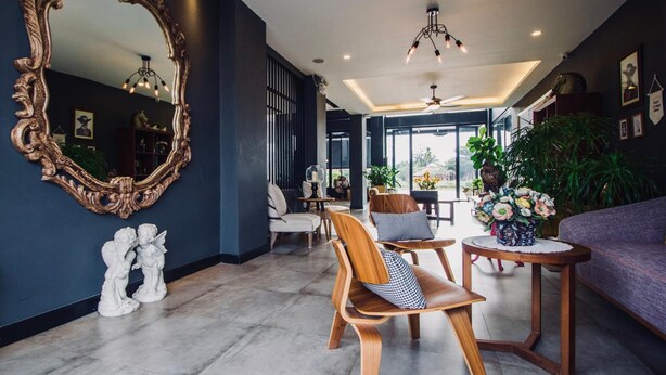 A modern interior with a large ornate mirror, wooden chairs, a round table with a vase of flowers, and a purple sofa. - Hataara Hua Hin (Hua Hin)