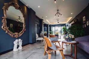 A modern interior with a large ornate mirror, wooden chairs, a round table with a vase of flowers, and a purple sofa. - Hataara Hua Hin (Hua Hin)