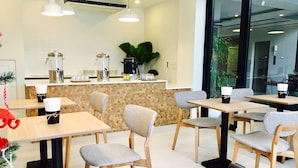 A modern cafe with wooden tables and chairs, a counter with coffee-making equipment, and a large window offering a view of the outdoors. - Hataara Hua Hin (Hua Hin)