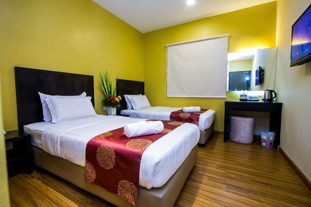 Habitación de hotel con dos camas, un escritorio, una silla, un cubo de basura y una ventana.