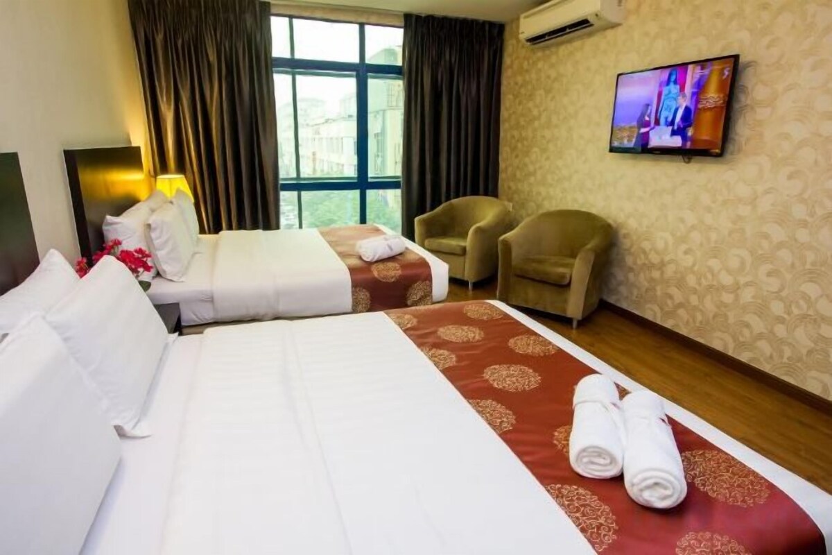 Habitación de hotel con dos camas, televisión, una silla y ventana con cortinas.