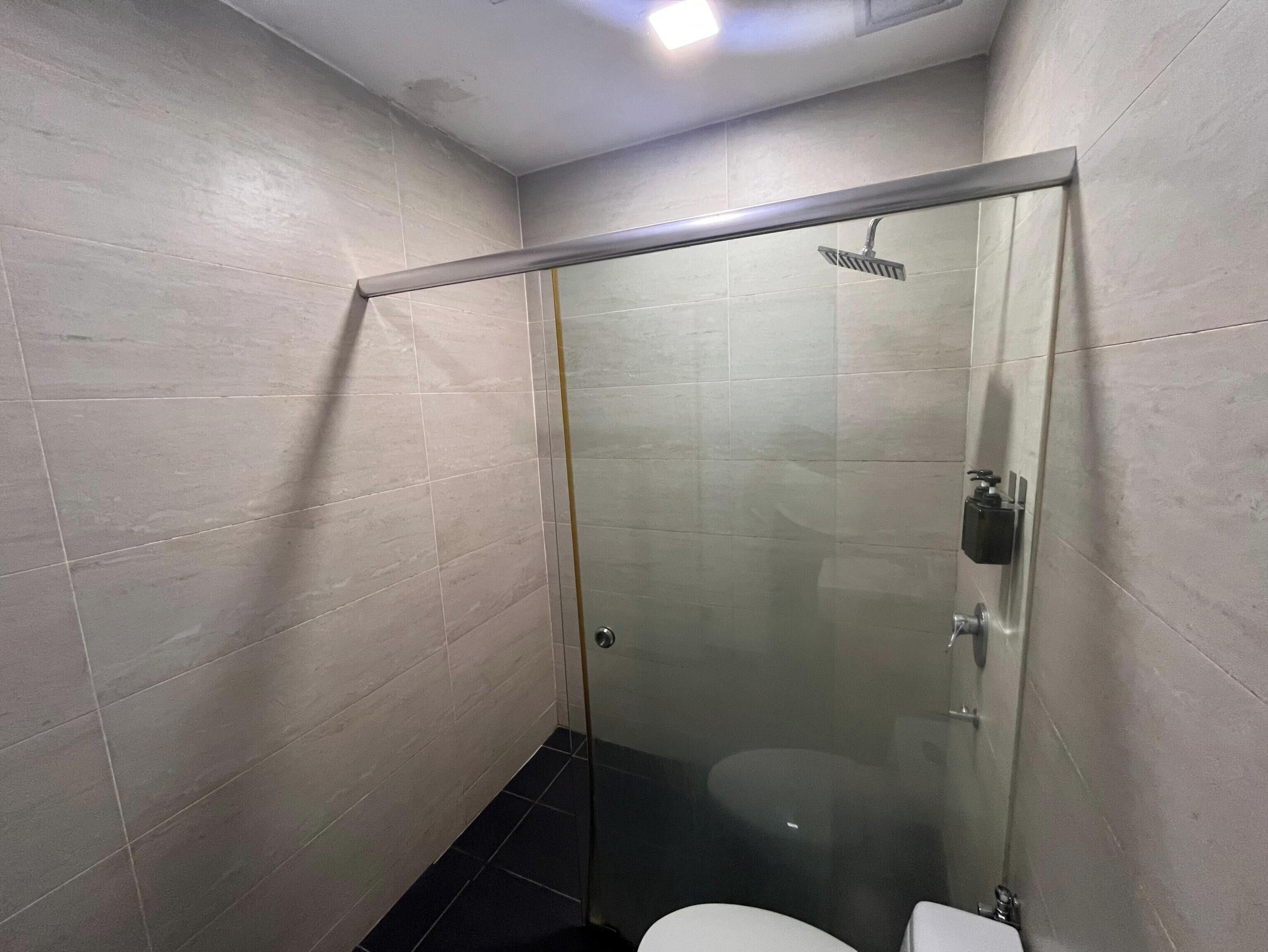 Een douchecabine met glazen wanden, een toilet, betegelde muren en een zichtbare douchekop.