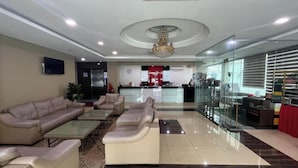 A hotel lobby with a reception desk, seating area with sofas and a coffee table, and a glass partition wall. - Capital O 91074 Grand World Hotel (Masai)