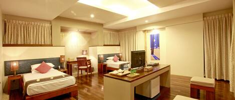A hotel room with a bed, desk, chair, and a small kitchenette area.