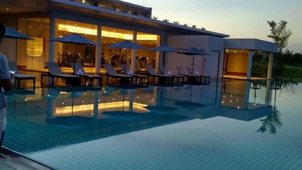 A modern hotel with a pool area featuring lounge chairs and umbrellas, a glass-enclosed structure, and a reflection pool. - The Thingaha Nay Pyi Taw (Naypyidaw)