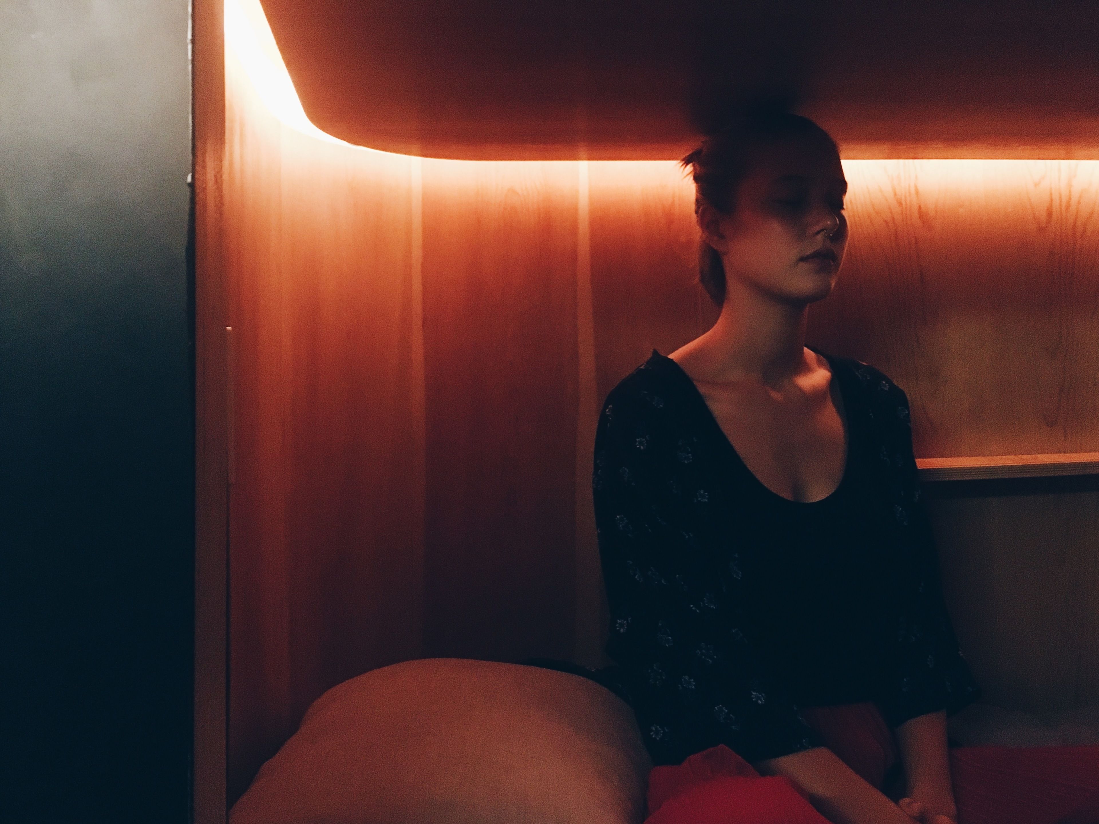 A person sitting in a dimly lit room with wooden walls and a bench.
