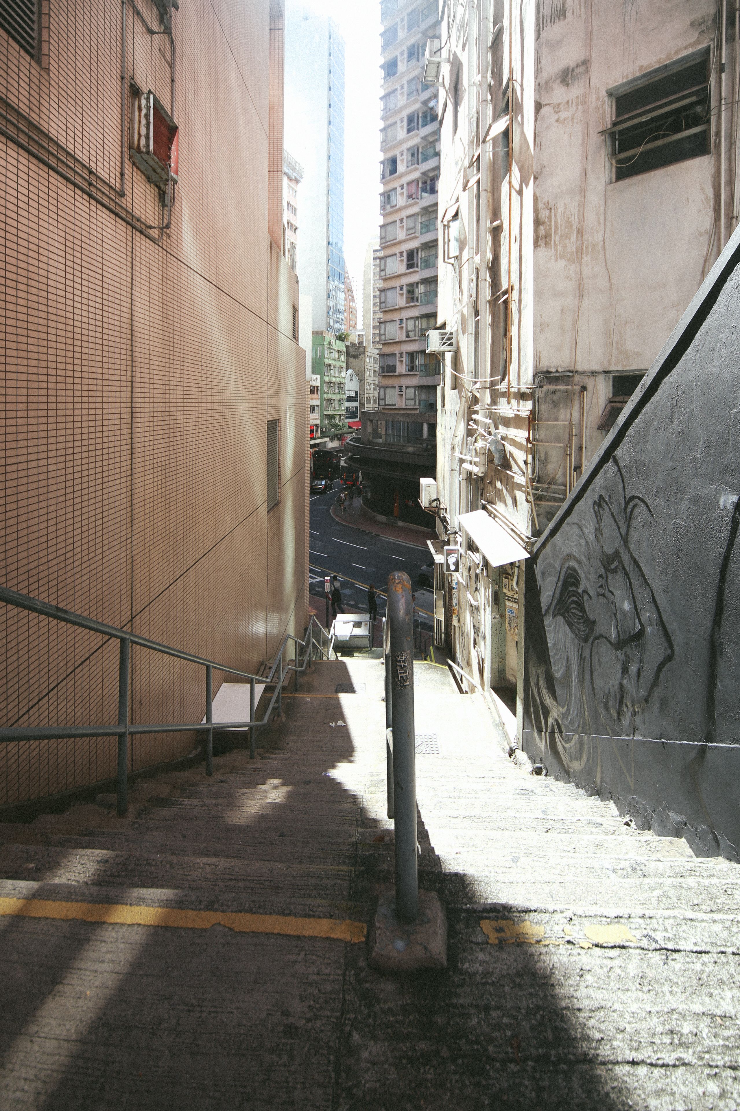 A narrow urban street with a metal railing and a graffiti-covered wall.