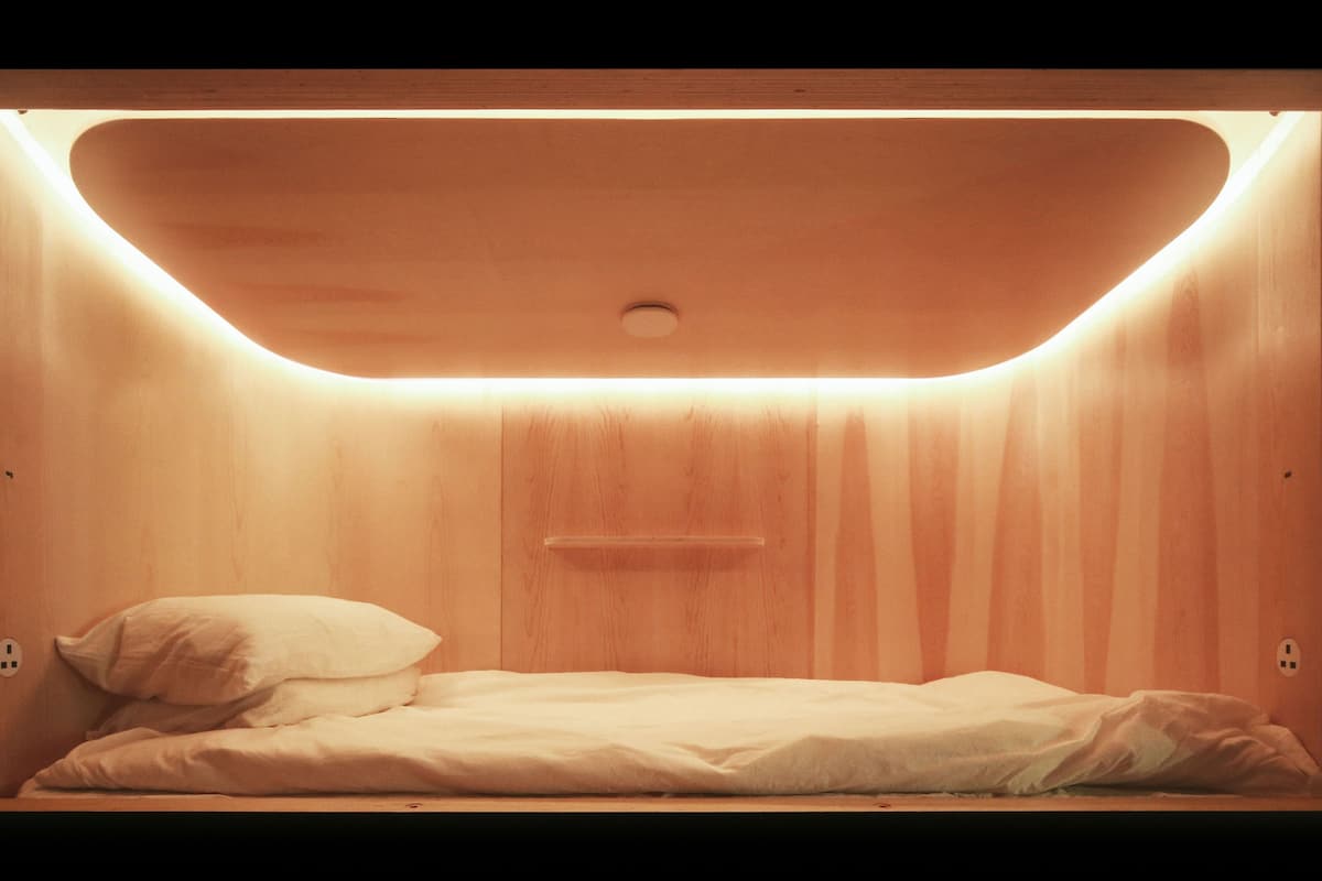 Un cuarto pequeño y cerrado de madera, con una cama, un estante y un enchufe.