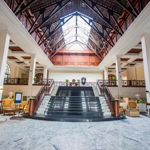 Eine prachtvolle Hotelhalle mit Marmorboden, einer zentralen Treppe und einer hohen Decke mit Holzbalken.