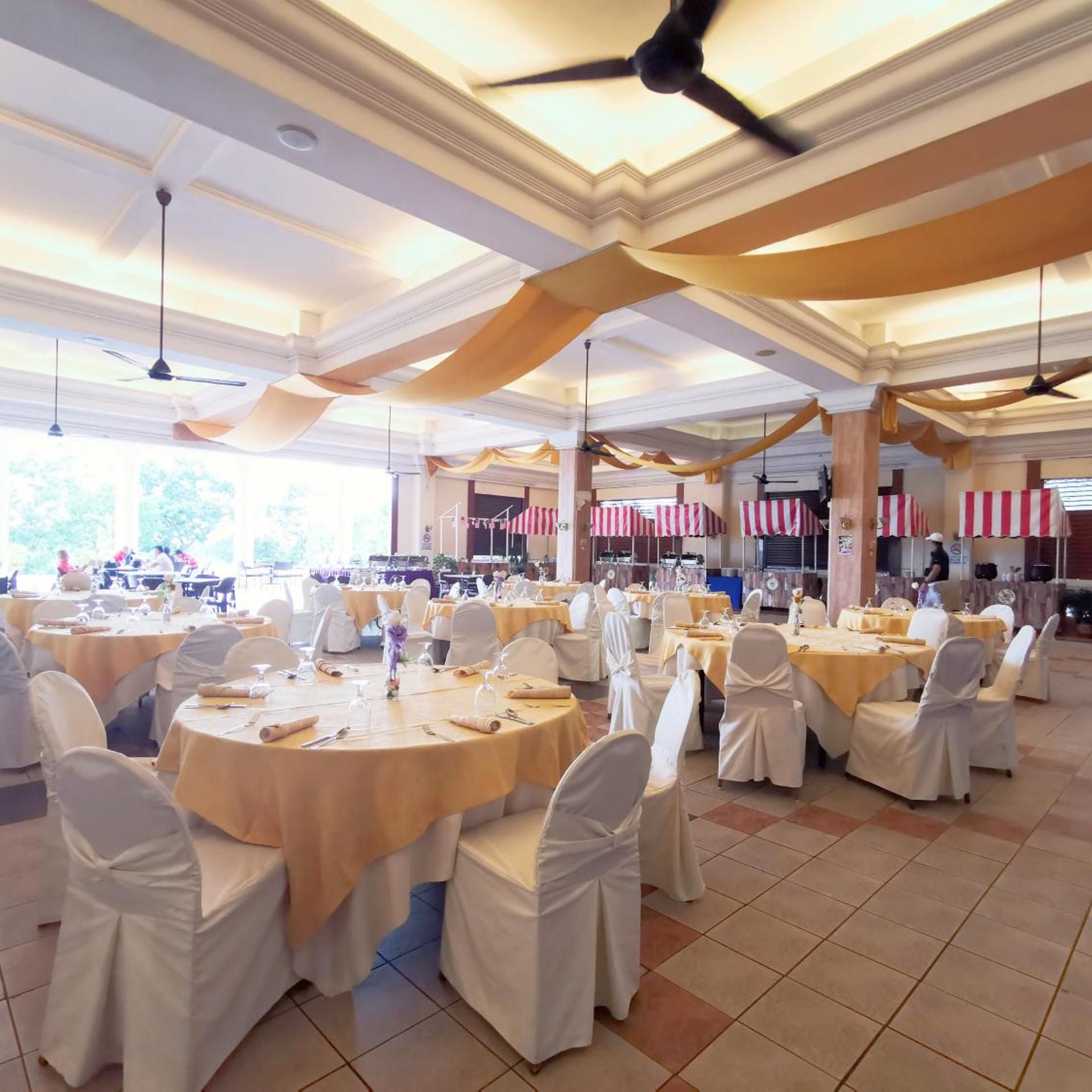 Un salón de banquetes con mesas redondas, sillas blancas y ventiladores de techo.