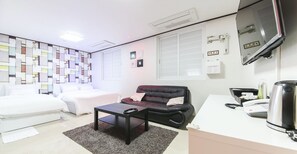 A modern hotel room with a bed, a black leather sofa, a small table, a desk with a telephone and a kettle, and a wall with a geometric pattern. - Itaewon A One Hotel (Seoul)