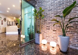 A reception area with a glass door, a brick wall, and potted plants. - Itaewon A One Hotel (Seoul)