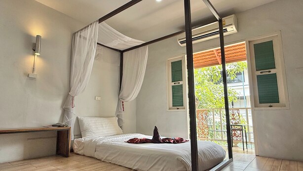 Un dormitorio con cama con dosel, una mesita de noche y vistas al exterior a través de una ventana con contraventanas verdes.