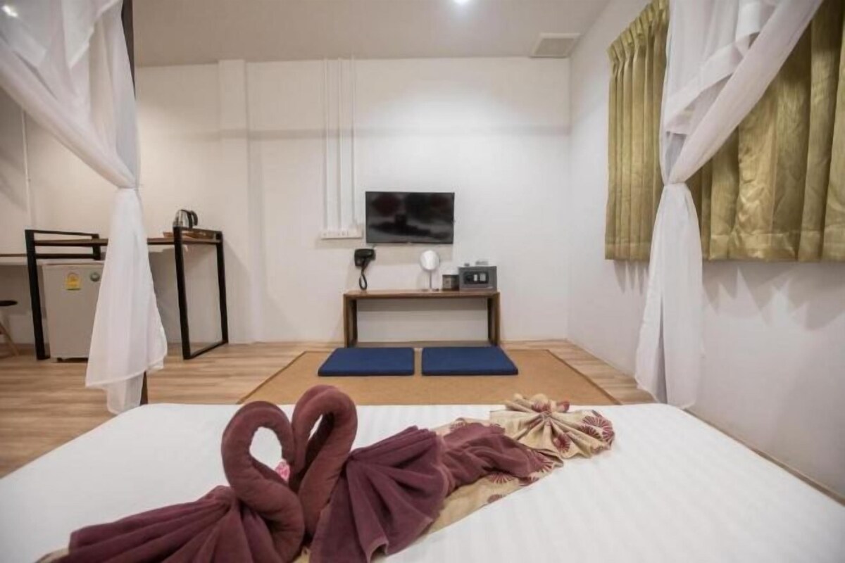 Una habitación de hotel con cama, escritorio, silla, televisor y ventana con cortinas.