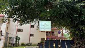 Entrada de hotel con un letrero para el Sabaidee Chumphon Hotel, acceso por un portón y un árbol con raíces expuestas.