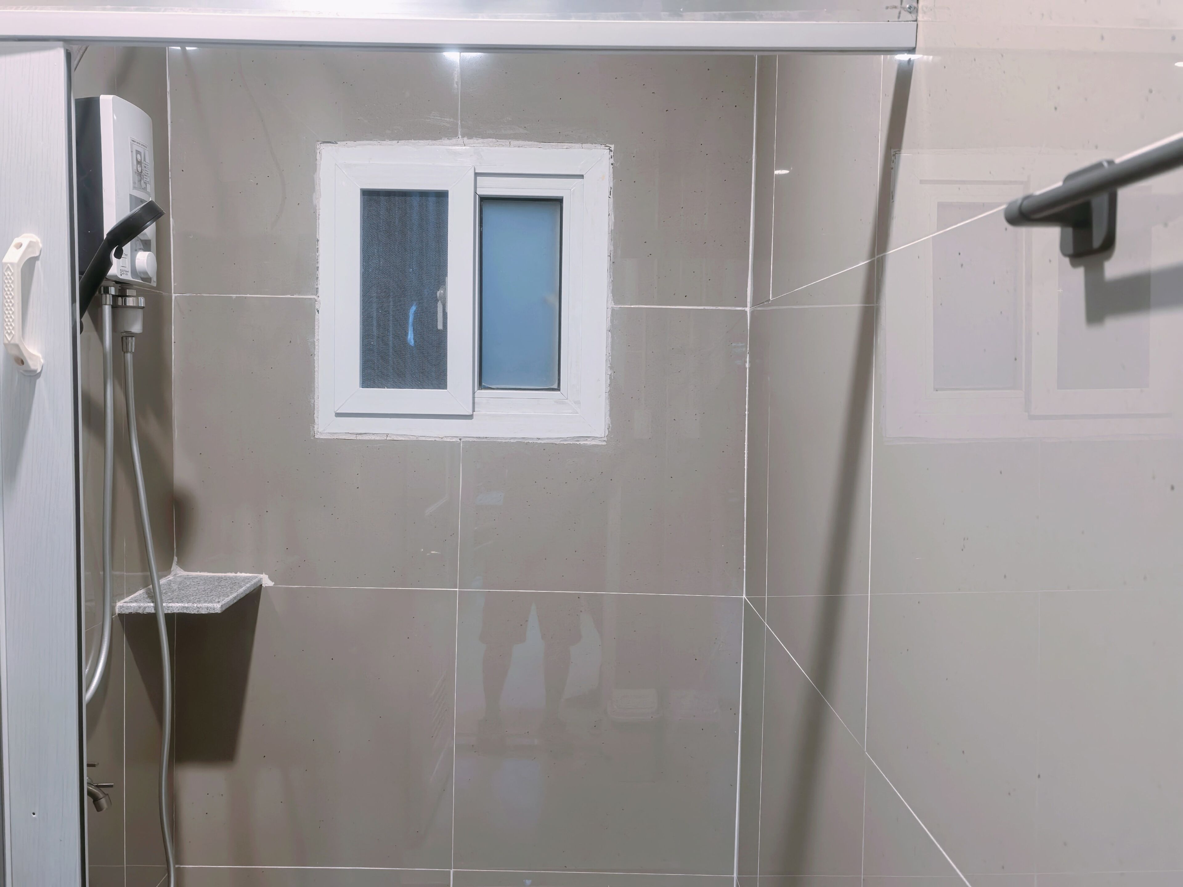 A bathroom with a shower, a small window, and a hand dryer.