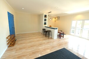 A spacious kitchen with a wooden floor, a blue door, and a bar area with stools.