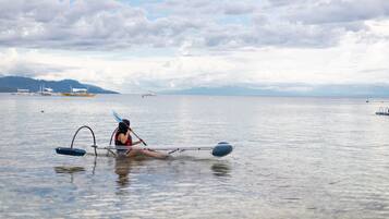 Une personne fait du kayak sur une étendue d’eau calme, avec une côte lointaine et des bateaux en arrière-plan.