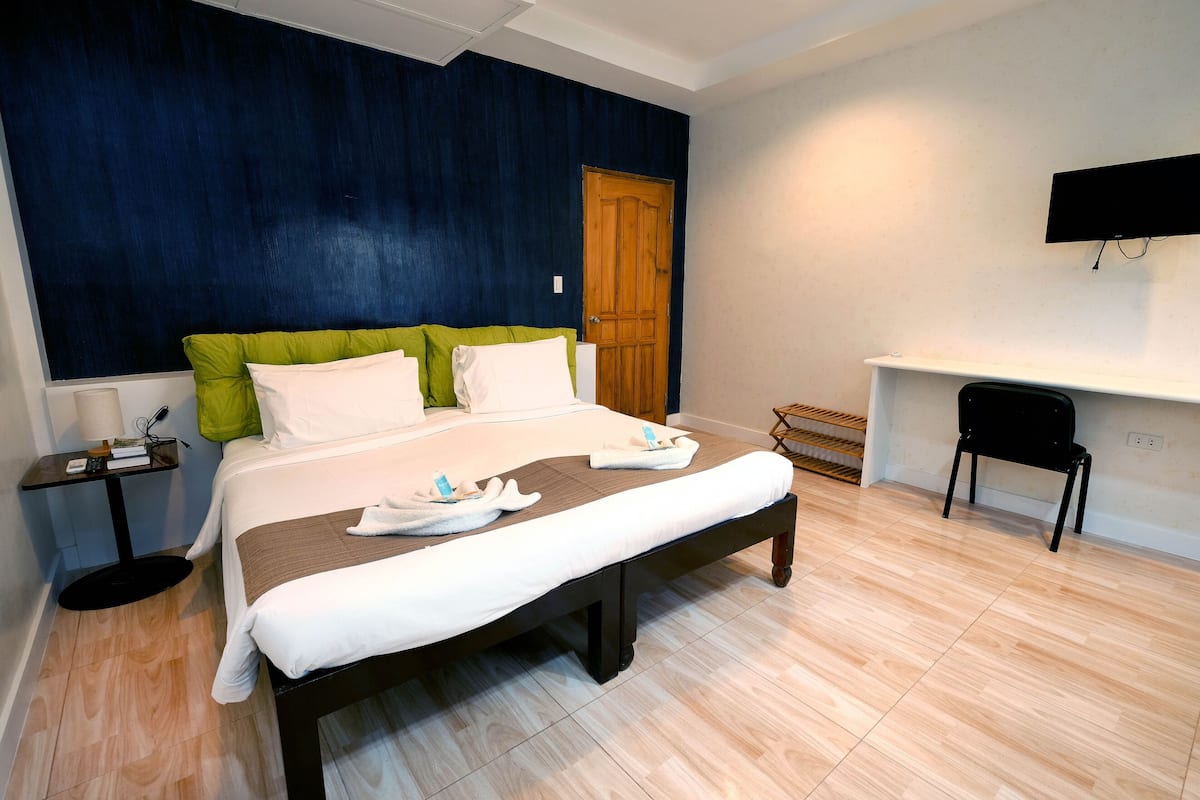 A hotel room with a bed, a desk, a chair, a TV, and a door.